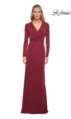 A woman wears a wine-colored La Femme 29535 long-sleeve formal dress featuring a floor-length V-neck silhouette and ruched waist detail.