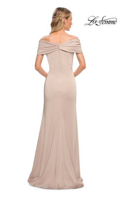 A woman models the Long Formal Dress: La Femme 29537, an off-the-shoulder, floor-length light beige gown. The fitted sheath design elegantly highlights her silhouette as she faces away, revealing the back details of the dress. The “La Femme” logo appears in the top right corner.