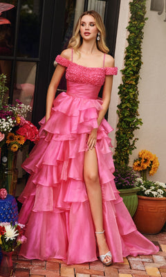 A woman in the Ava Presley 29544 Ruffled Prom Ball Gown, featuring a bright pink off-the-shoulder design with a princess a-line skirt and thigh-high slit, stands outdoors near flowers and greenery.