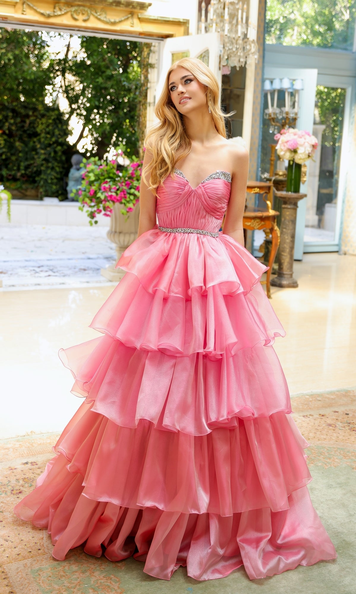 A woman stands indoors in the Long Prom Dress 29546 by Ava Presley, featuring a strapless sweetheart neckline, layered ruffle ball gown skirt, fitted bodice, and beaded detail, surrounded by elegant decor and greenery.