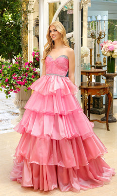 A woman stands indoors wearing the Long Prom Dress 29546 by Ava Presley, a strapless sweetheart ball gown with layered ruffles and silver embellishments, surrounded by flowers and ornate decor.