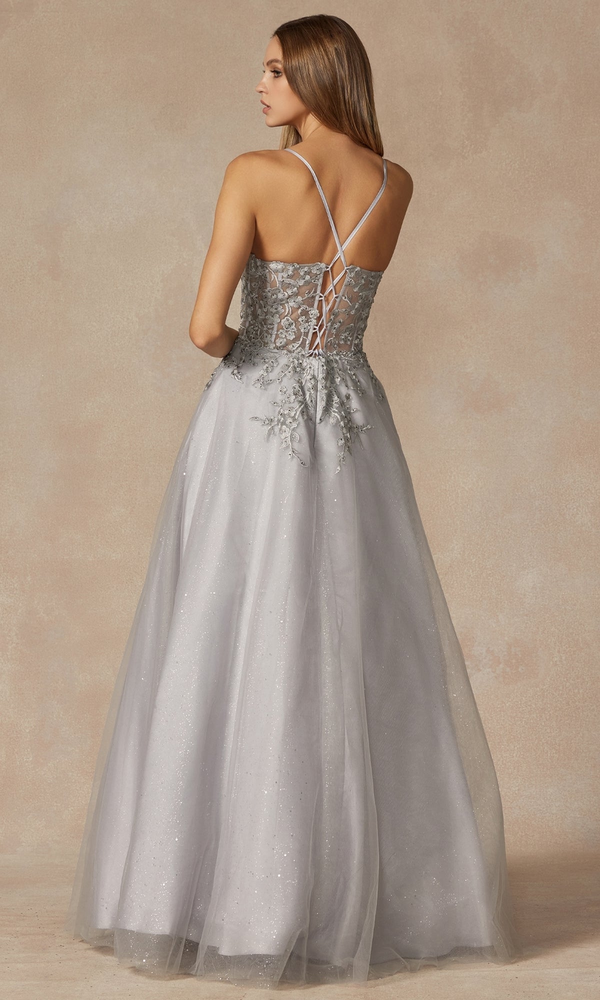 A woman models the Juliet 295 Lace-Up Long A-Line Prom Dress, featuring crisscross straps and embroidered floral designs, against a neutral background.