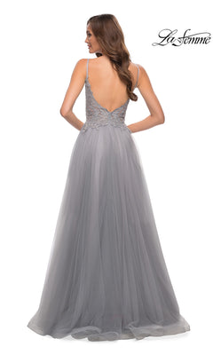 A woman stands with her back to the camera in a light gray La Femme Lace-Bodice Long A-Line Prom Dress 29686, featuring an embroidered lace bodice, deep V-back, and flowing tulle skirt.