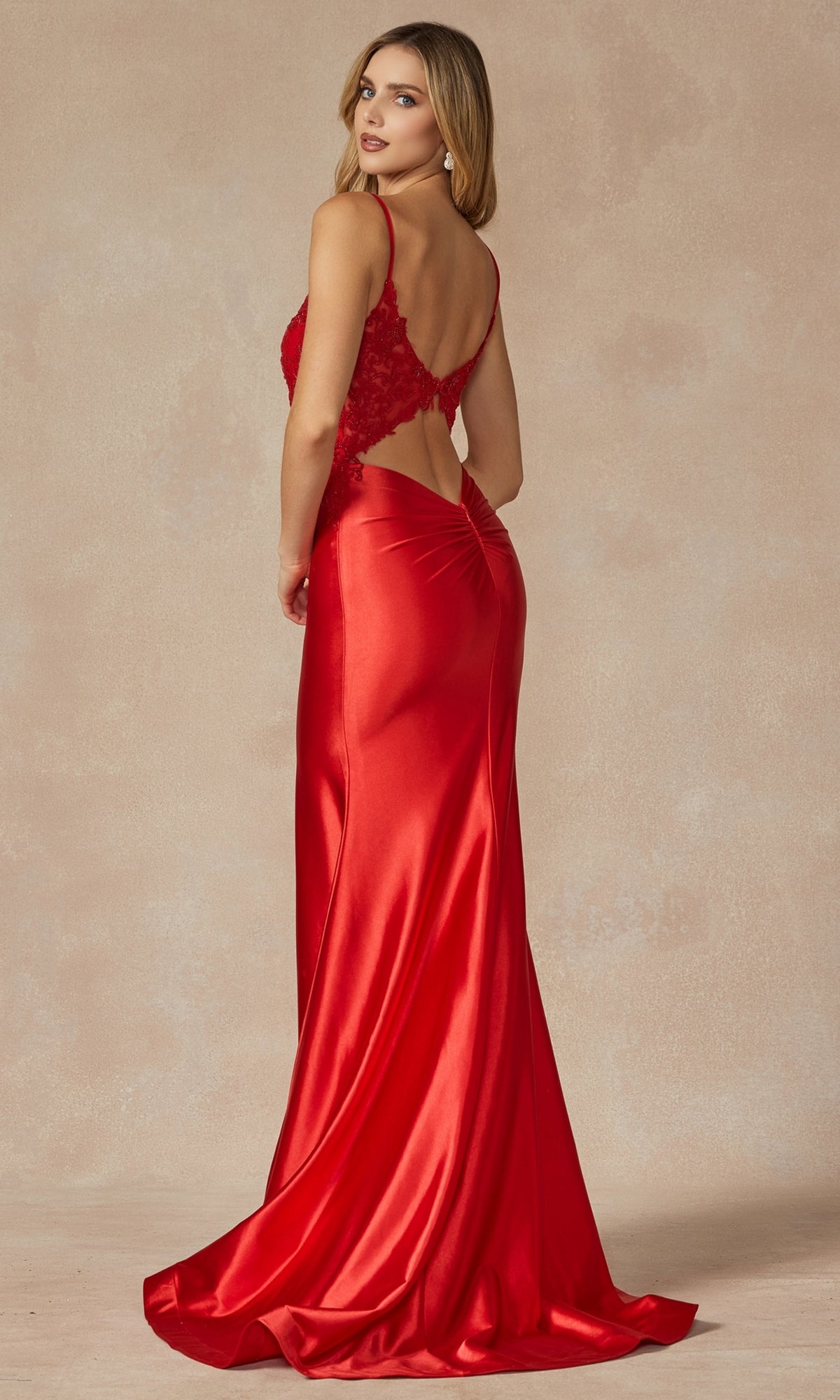 A woman faces away, wearing the Long Prom Dress 296 by Juliet—a fitted, floor-length red gown with an open back and elegant lace detailing—set against a neutral background.