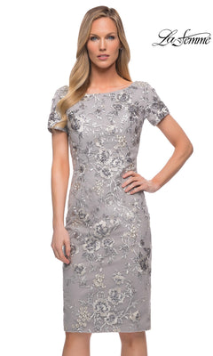 A woman models the Knee Length Wedding Guest Dress: La Femme 29824 with metallic floral-lace embroidery, posing in front of a plain white background. The “La Femme” logo is top right.