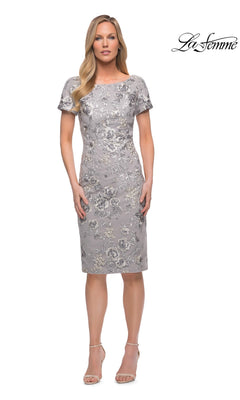 Woman wearing Knee Length Wedding Guest Dress: La Femme 29824 in silver with floral lace and short sleeves, paired with nude heels. La Femme logo shown top right against white background.