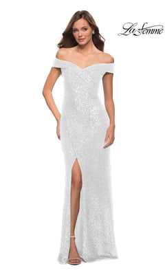 A woman wears the La Femme Long Prom Dress 29831—a white, off-the-shoulder, floor-length sequin gown with a front slit—paired with silver heels, posing against a plain white background.