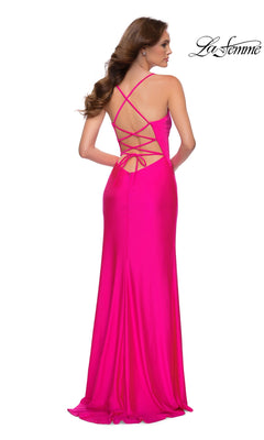 A woman models the La Femme Hot Pink Long Prom Dress 29870, featuring an open back with crisscross straps, standing against a white background.