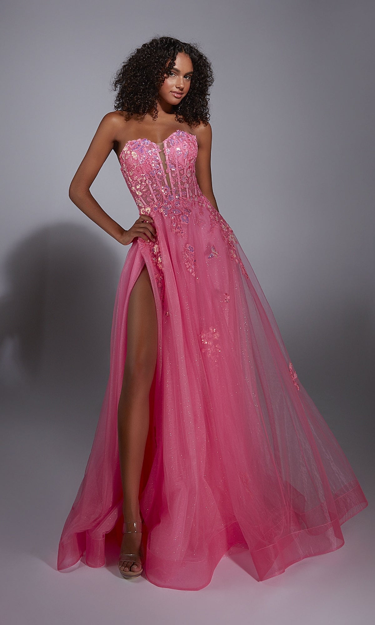 A woman models the Aerie Couture 298 Glitter Tulle Prom Ball Gown—pink, strapless, with floral lace embroidery and a thigh-high slit—standing against a plain gray background.