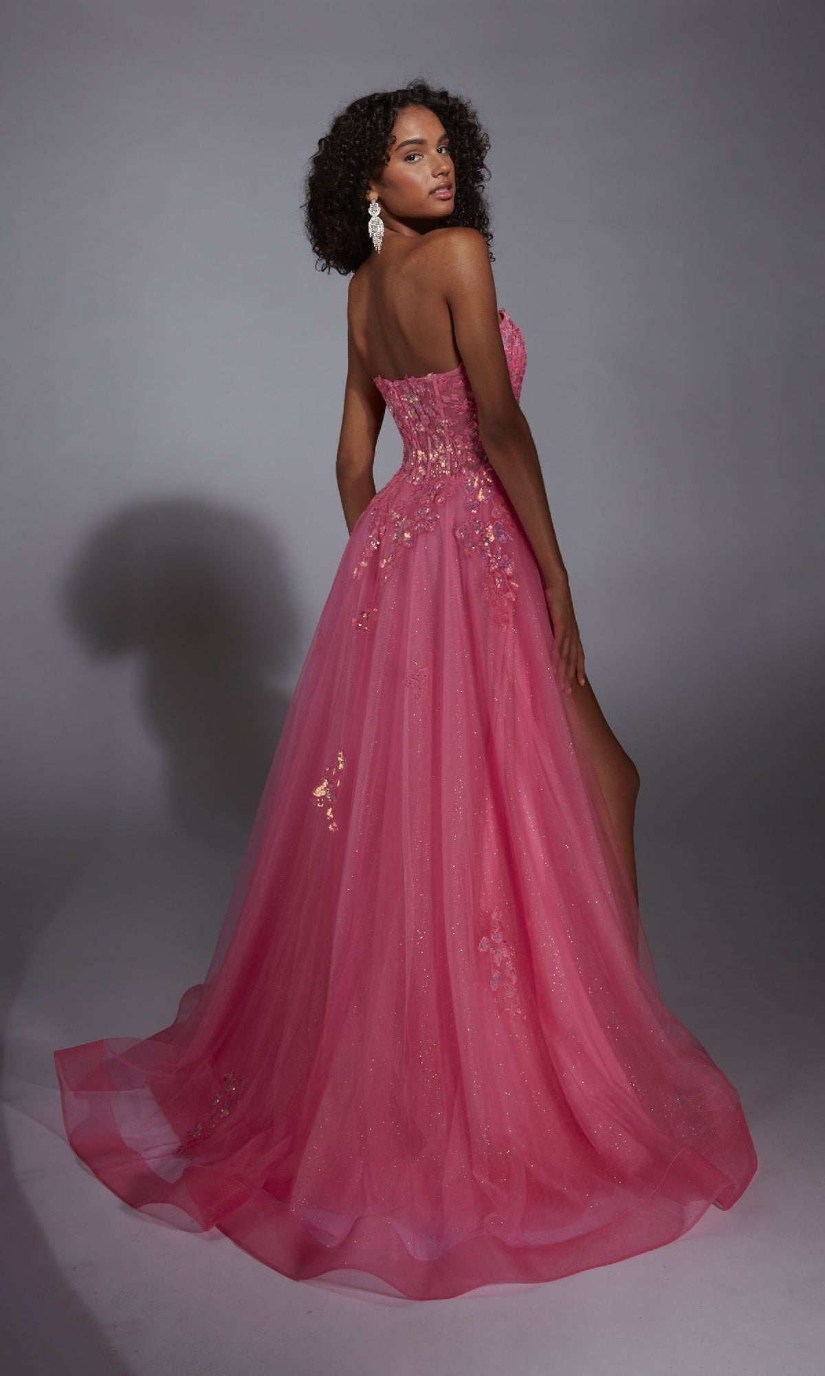 Woman in the Glitter Tulle Prom Ball Gown: Aerie Couture 298, a pink strapless dress with floral lace embroidery, stands against a plain gray background and gazes over her shoulder.