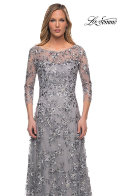 Model in Long Formal Dress: La Femme 29903—silver, modest style with metallic floral lace and three-quarter sleeves—stands against a white background; “La Femme” logo top right.