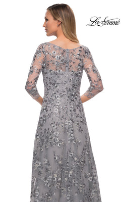 Woman in a silver Long Formal Dress: La Femme 29903 with metallic floral lace, sheer sleeves, and back panel, facing away. “La Femme” logo at upper right.