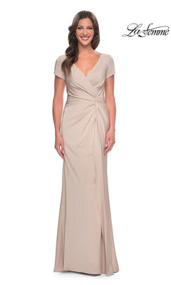 A woman wearing a Long Formal Dress: La Femme 29926, featuring a floor-length, beige V-neck gown with short sleeves and a twist-knot waist detail.