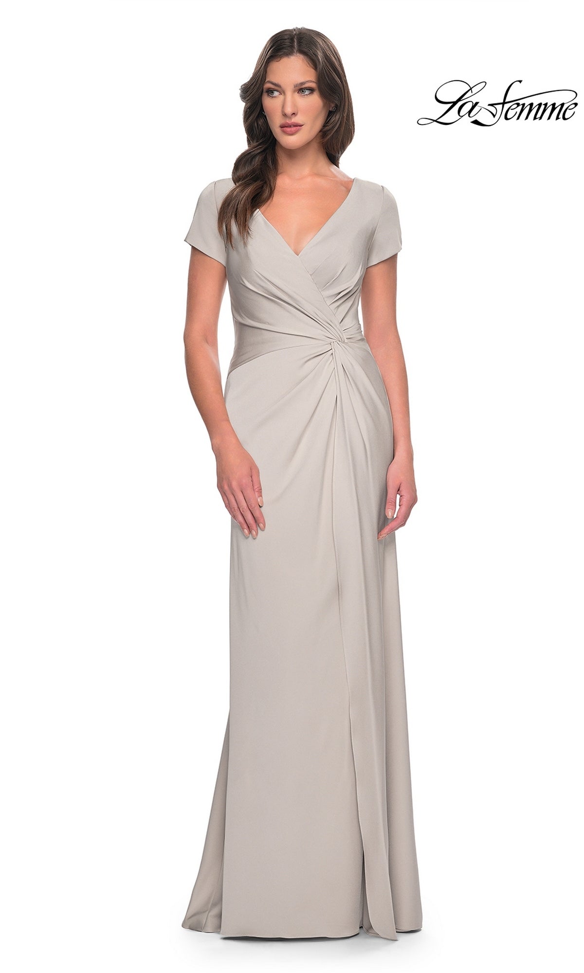 A woman wears a silver Long Formal Dress: La Femme 29926 featuring a V-neck, short sleeves, a twist-knot detail, and a floor-length hem.