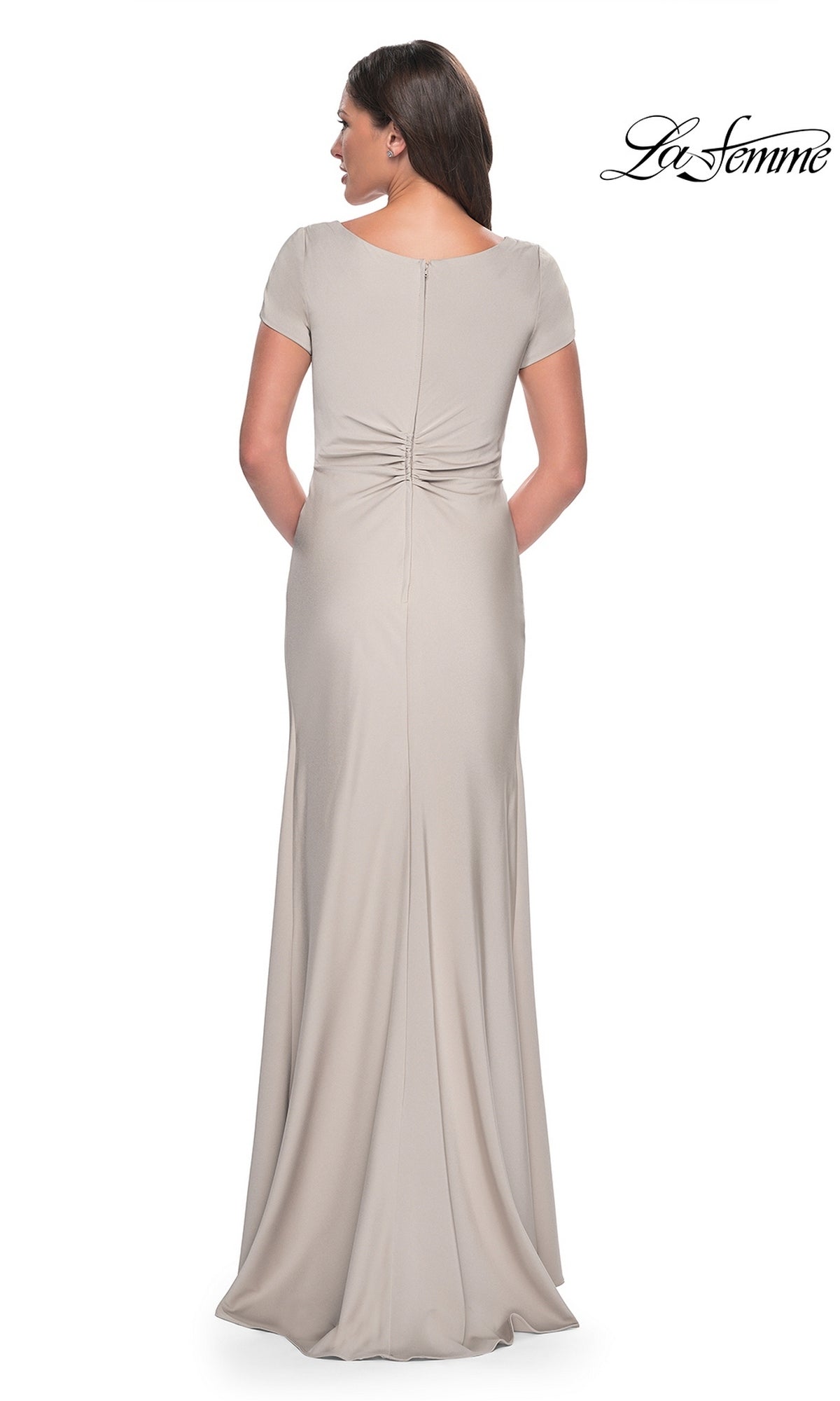 A woman seen from behind wearing the beige Long Formal Dress: La Femme 29926, featuring short sleeves and a ruched twist-knot detail at the lower back.