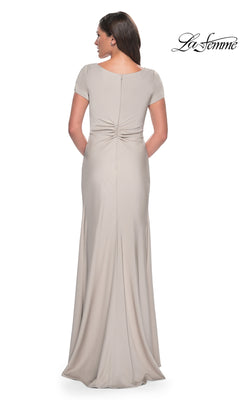 A woman seen from behind wearing the beige Long Formal Dress: La Femme 29926, featuring short sleeves and a ruched twist-knot detail at the lower back.