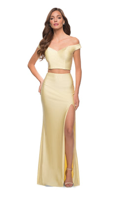 A woman confidently poses with one hand on her hip, wearing the Off-the-Shoulder Two-Piece Prom Dress: La Femme 29951 in light yellow, featuring a high slit and stylish off-the-shoulder design.