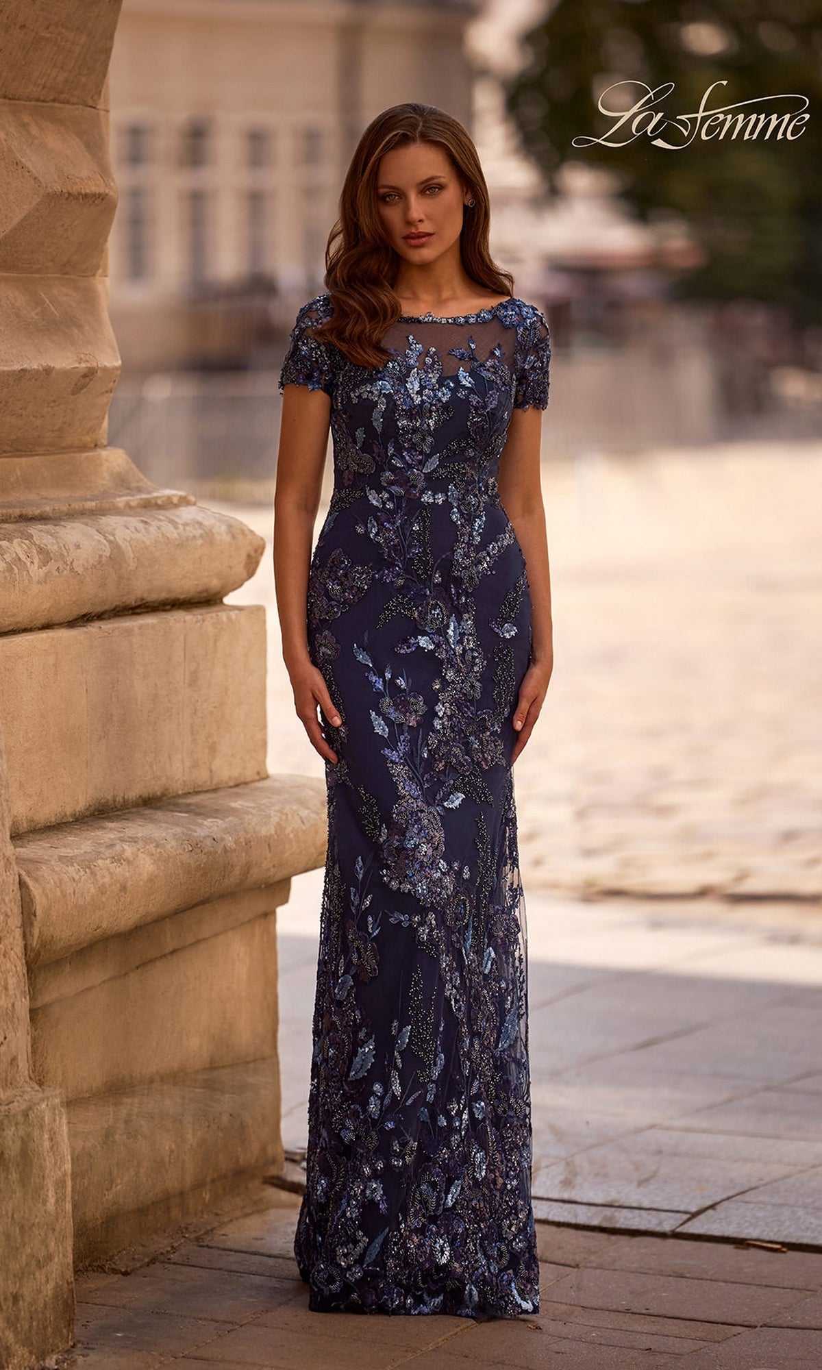 Woman outdoors by a stone building wearing Long Formal Dress: La Femme 29961 in navy, a sequin-beaded sheath evening gown with silver and purple embellishments.