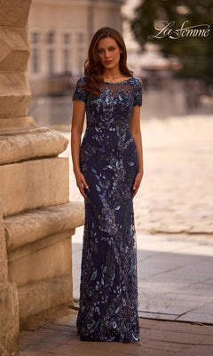 Woman outdoors by a stone building wearing Long Formal Dress: La Femme 29961 in navy, a sequin-beaded sheath evening gown with silver and purple embellishments.