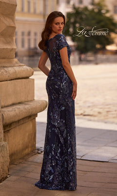 A woman in a dark blue, floor-length sheath gown stands outdoors with buildings behind. Long Formal Dress: La Femme 29961 appears in the upper right corner.
