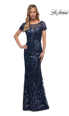 A woman in a fitted navy sheath covered in floral sequin embroidery poses with one hand on her hip. Long Formal Dress: La Femme 29961.
