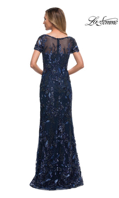Woman in Long Formal Dress: La Femme 29961, navy blue sheath gown with sheer back and sequin floral embroidery, standing with her back to the camera.