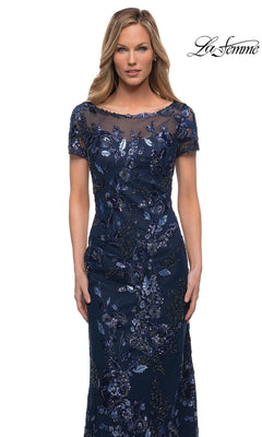 Woman wearing Long Formal Dress: La Femme 29961—navy blue sheath evening gown with floral embroidery and sheer neckline. “La Femme” logo in the top right corner.
