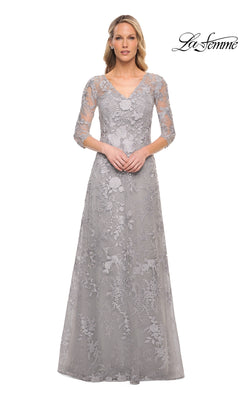 A woman wears the Long Formal Dress: La Femme 29989, a floor-length, silver formal gown with a V-neck, three-quarter sleeves, and floral lace embroidery.