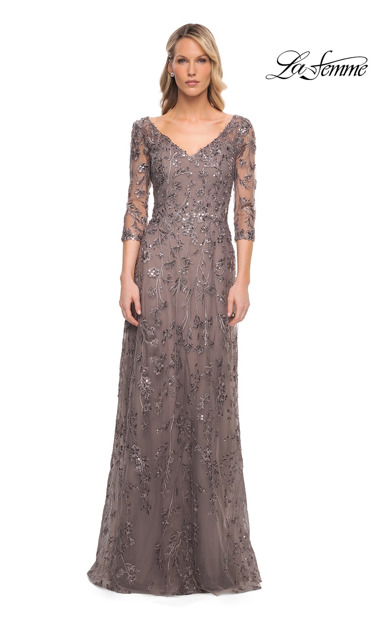 A model wearing the Long Formal Dress: La Femme 29994, a floor-length, taupe V-neck formal dress with sheer sleeves and sequin floral embroidery.