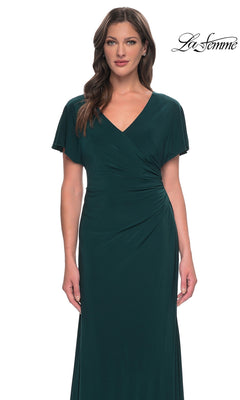 A woman wearing a dark green, V-neck La Femme 29997 formal dress with a sheath skirt and short, draped sleeves.