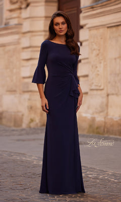 A woman in a floor-length, dark blue Bell-Sleeve Long Formal Dress (La Femme 29999) with flared sleeves stands on a cobblestone street in front of a stone building.