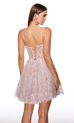 A woman stands with her back to the camera, wearing the Alyce 30003 short homecoming dress—a light pink floral A-line gown with a corset bodice, lace-up back, thin straps, and delicate floral embroidery.