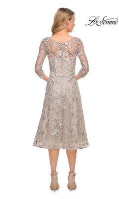 Back view of a woman wearing the Midi Wedding Guest Dress: La Femme 30004, a champagne-colored, three-quarter sleeve lace midi dress with floral embroidery and sheer accents, paired with ankle-strap heels.