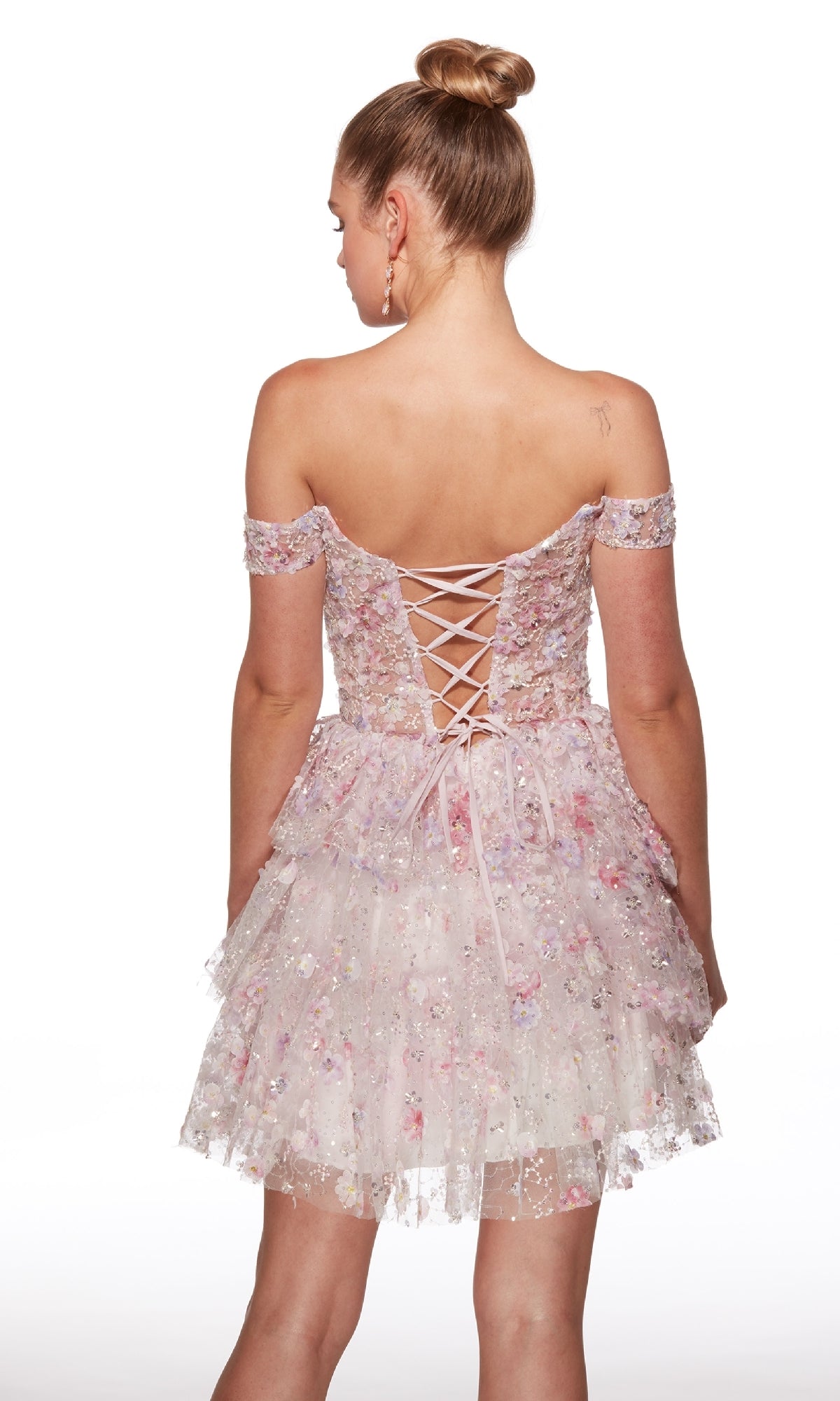 A woman faces away, showing the lace-up back of the Alyce 30004 short homecoming dress—a light pink, off-the-shoulder fit-and-flare style with floral patterns.