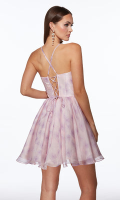 A woman stands against a white background wearing the Alyce 30006 Short Fit-and-Flare Print Hoco Dress, featuring a light purple floral print, lace-up back, and crisscross straps.