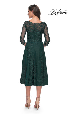 A woman wearing a dark green, modest lace Midi Wedding Guest Dress: La Femme 30016 with three-quarter sleeves and floral embroidery, paired with nude high-heeled pumps.
