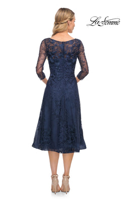 Back view of the navy blue, tea-length A-line La Femme 30016 lace dress with three-quarter sleeves and a boat neckline, worn with nude heels.