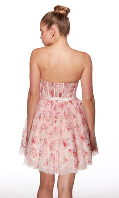 A woman faces away from the camera, wearing the Alyce 30019 short homecoming dress in a pink floral print with a strapless corset bodice and flared fit-and-flare skirt.