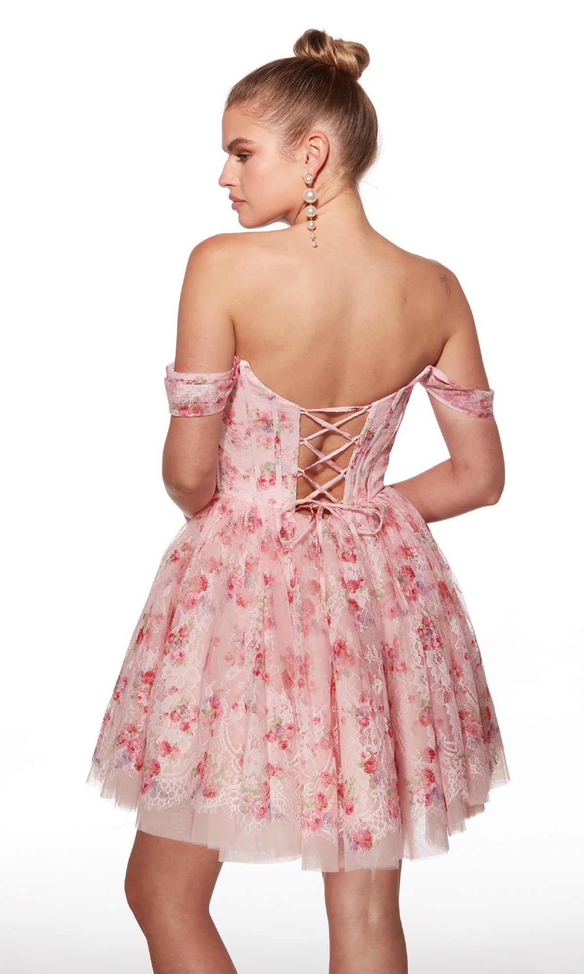 A woman stands against a white background wearing the Alyce 30021 Off-Shoulder Short Print Hoco Dress featuring pink floral lace and a corset-style lace-up back.