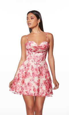 A woman models the Alyce 30033 short homecoming dress—a sleeveless, fit-and-flare style with thin straps, a sweetheart neckline, and pink floral patterns—while standing against a white background.