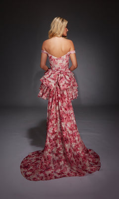 A woman stands facing away against a dark background, wearing the Alyce 30034 short homecoming dress—an off-the-shoulder, pink and white floral fit-and-flare style with ruffled layers.