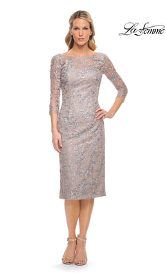 A woman wears the taupe, midi-length Midi Wedding Guest Dress: La Femme 30036, featuring three-quarter sleeves and an intricate floral lace overlay, paired with nude ankle-strap heels.