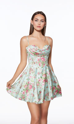 A woman wears the Alyce 30043 Short Homecoming Dress—a light blue, floral print fit-and-flare style with thin straps and a flared skirt—standing against a plain white background.