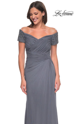 Woman in Long Formal Dress: La Femme 30057 featuring an off-the-shoulder beaded top, pleated bodice, and side-gathered skirt, standing and smiling. “La Femme” logo at top right.