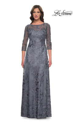A woman wears a slate-colored La Femme 30060 long formal dress featuring a sheer lace overlay, three-quarter length sleeves, and a scoop neckline.