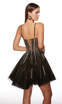 Woman wearing the Short Homecoming Dress: Alyce 30085, a black sleeveless fit and flare dress with rhinestone accents, flared short skirt, and lace-up back—standing and looking over her shoulder.