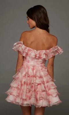 A woman facing away wears the Alyce 30089 short homecoming dress, featuring a ruffle tiered design with an off-shoulder pink and white layered skirt, set against a plain gray background.
