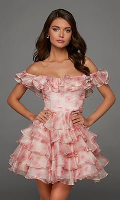 A woman poses with hands on hips against a plain gray background, wearing the Alyce 30089 short homecoming dress—a ruffled, off-the-shoulder pink floral organza design.