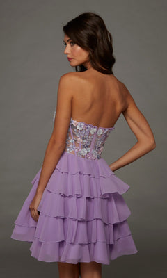 A woman stands in profile against a plain gray background, wearing the Alyce 30109 Short Homecoming Dress—a strapless lilac fit-and-flare party dress adorned with intricate 3D floral appliques on the bodice and ruffled layered detailing.