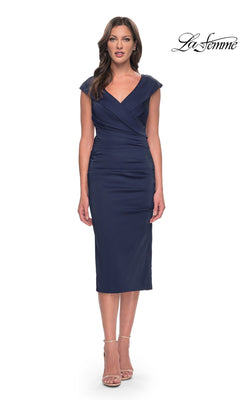 A woman wearing a navy blue Midi Wedding Guest Dress: La Femme 30110, featuring a fold-over V-neckline, cap sleeves, and neutral ankle-strap heels.